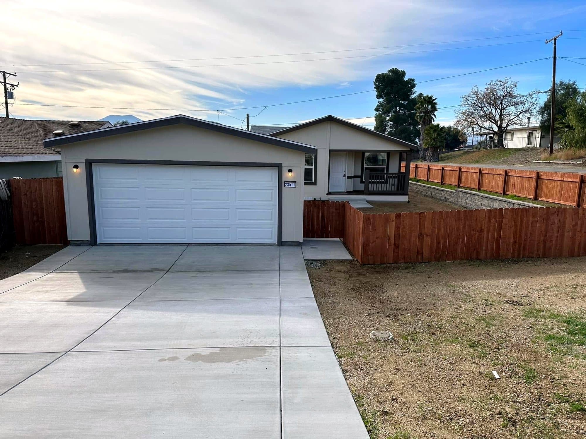 Beige manufactured home with a white garage door and wood fence