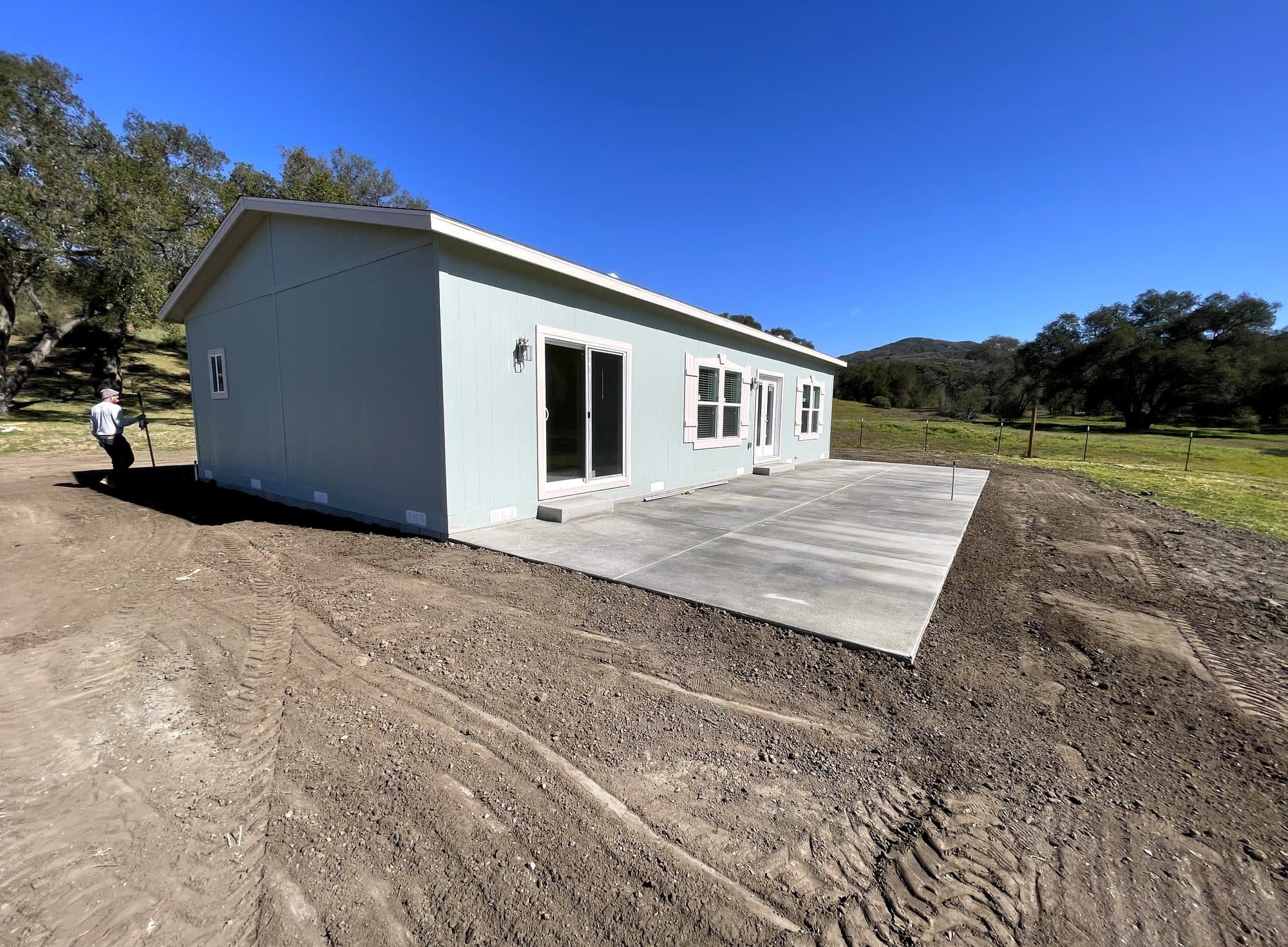 Pale green manufactured home set on a concrete pad among oak trees